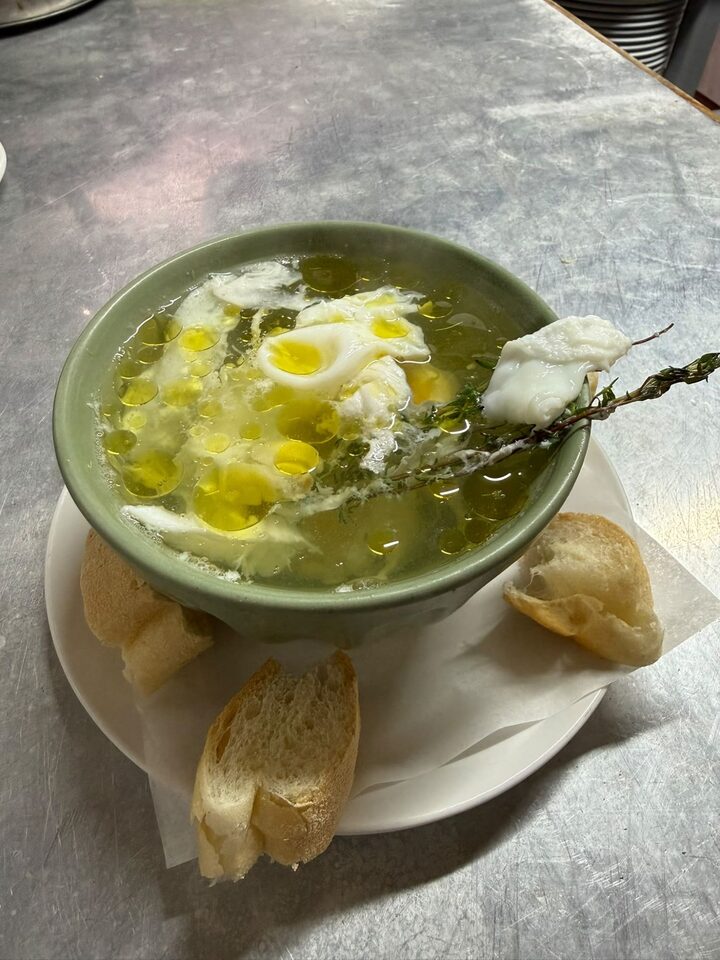 A bowl of soup with a poached egg and fresh thyme, served with bread
